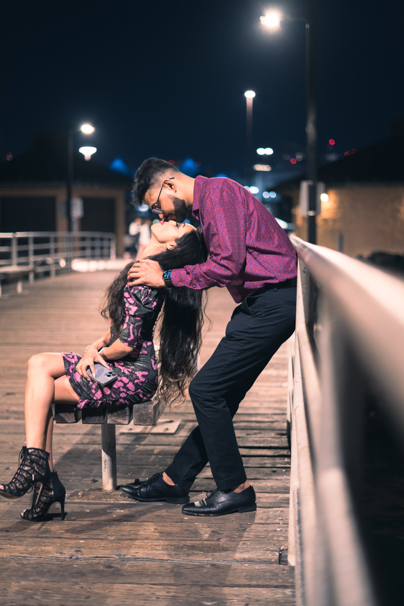 A dip kiss on a pier bench at night